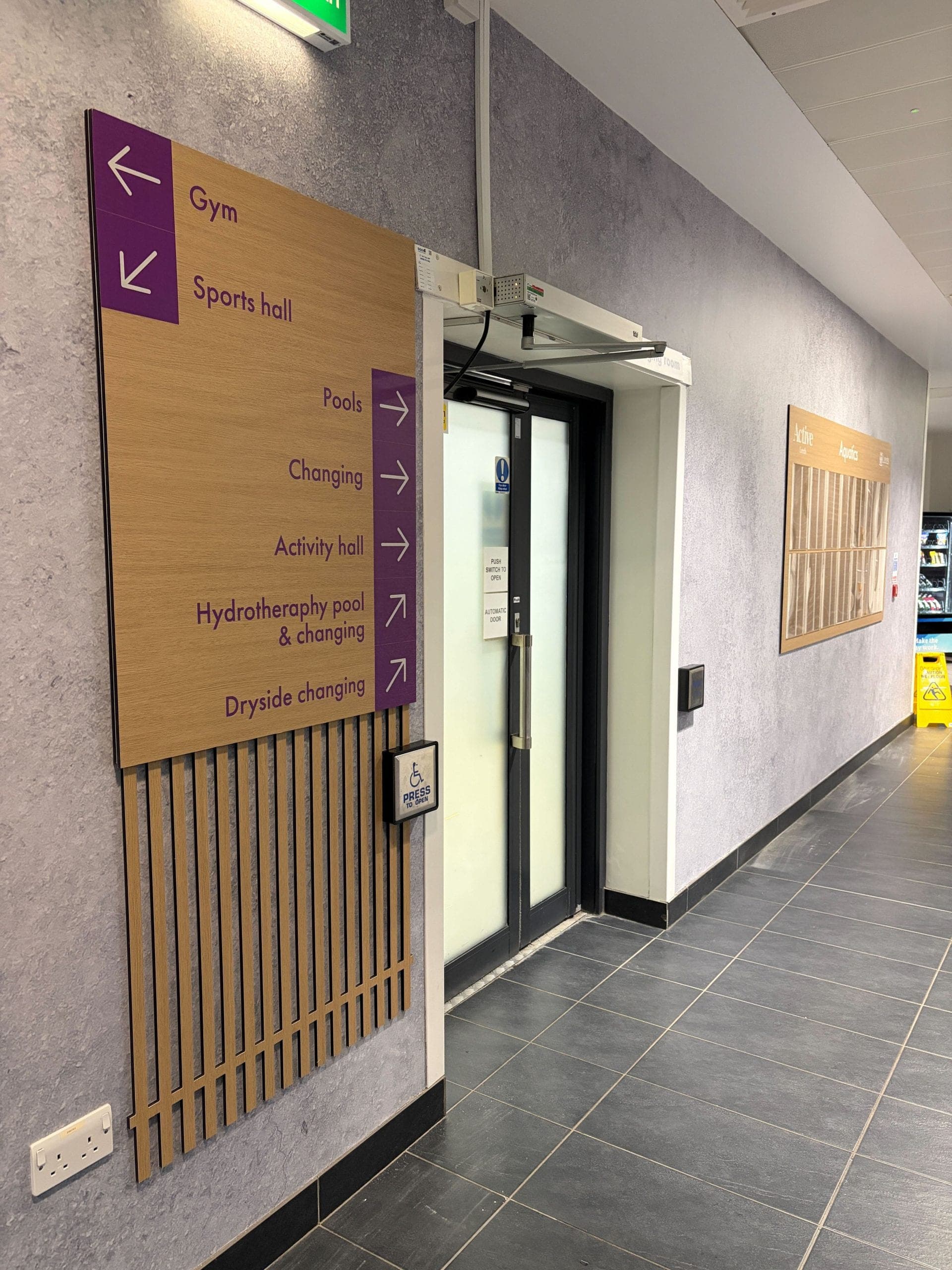 Directional wayfinding totem with chevron markers pointing to gym, pools, and changing facilities