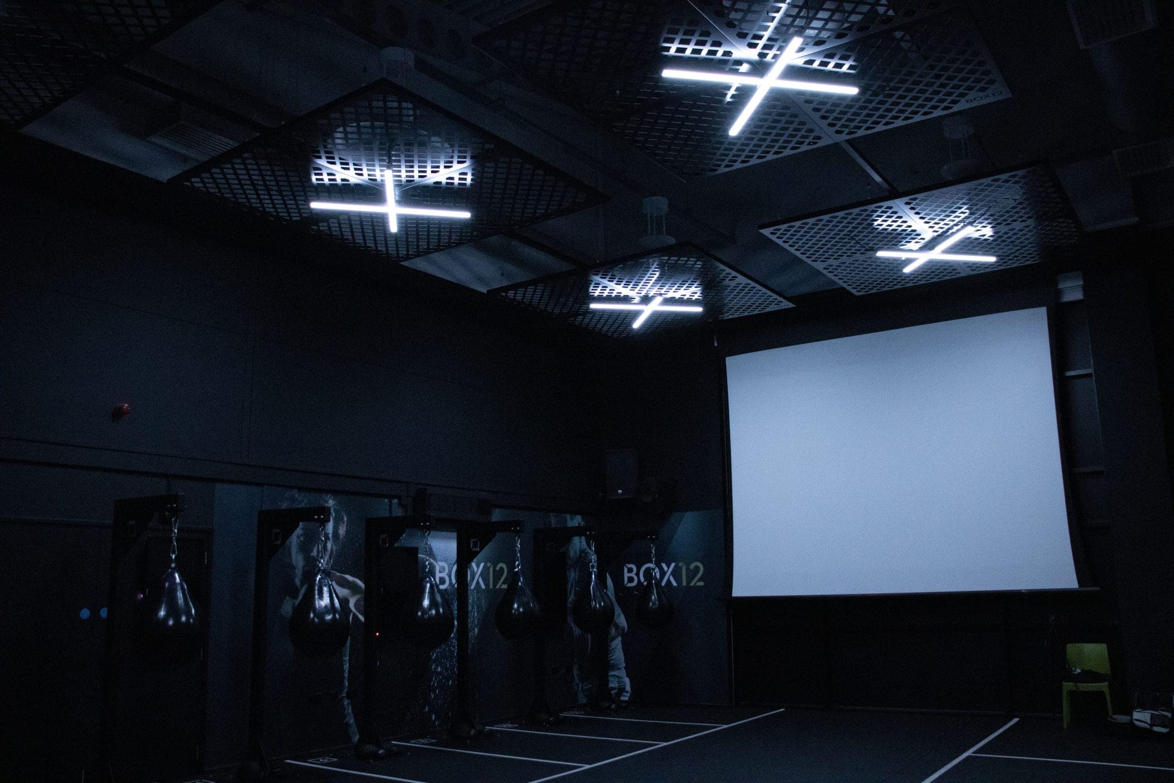 BOX12 boxing studio with punching bags, branded bays, large projection screen and white LED ceiling lights