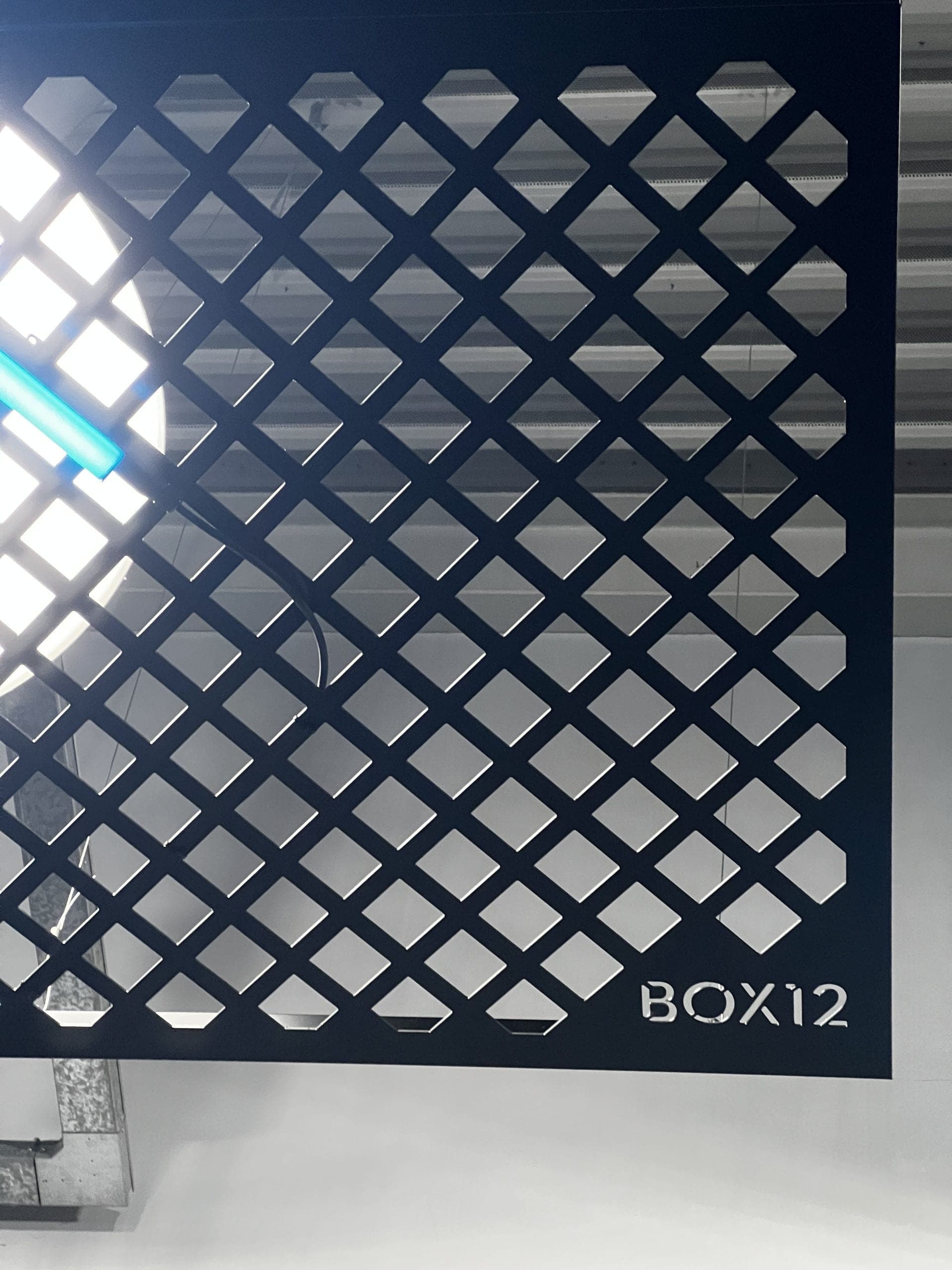 Close-up of dark diamond-pattern perforated metal panel with BOX12 text etched in corner