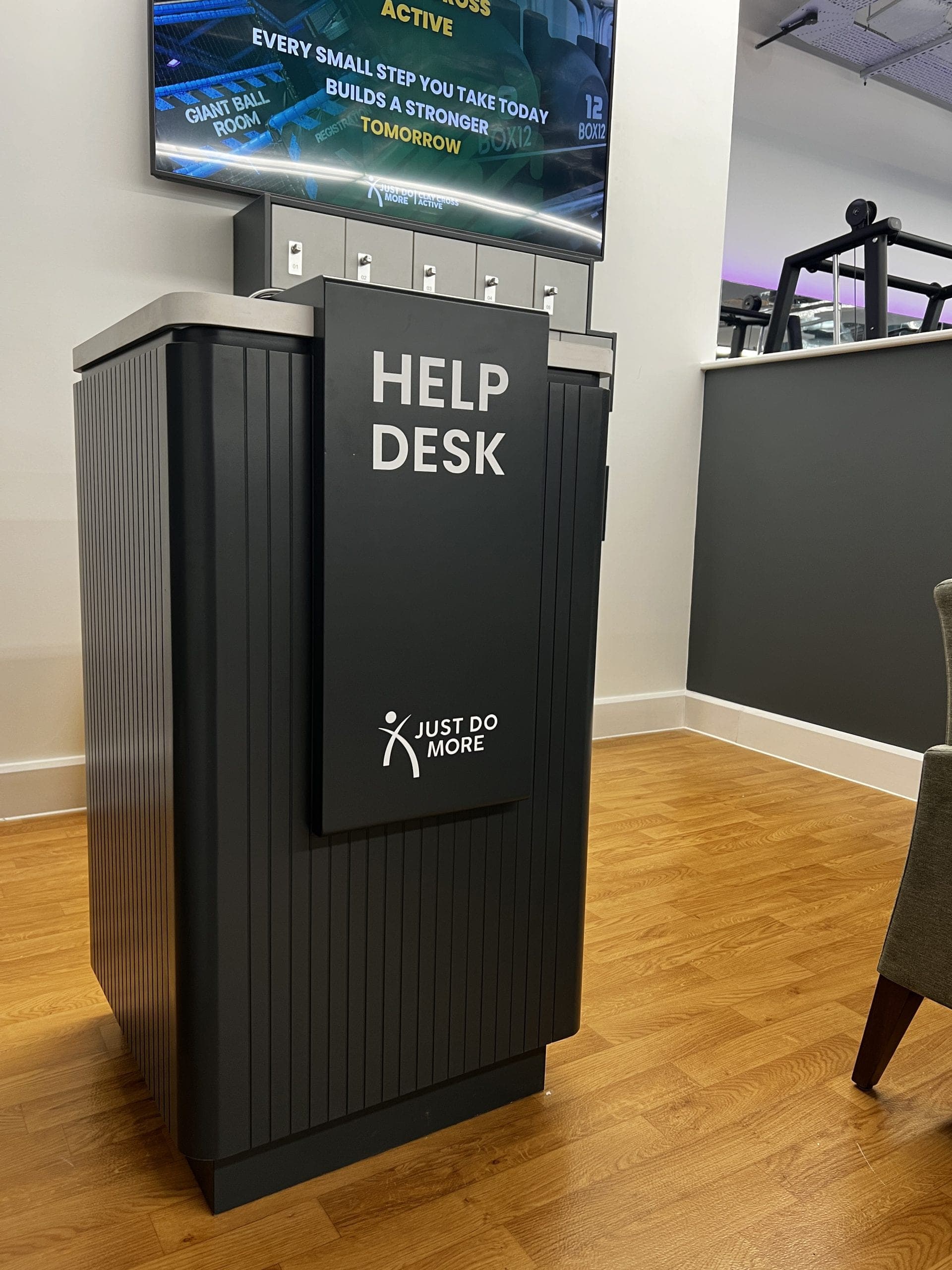 Freestanding branded Help Desk kiosk unit with digital screen above showing motivational content
