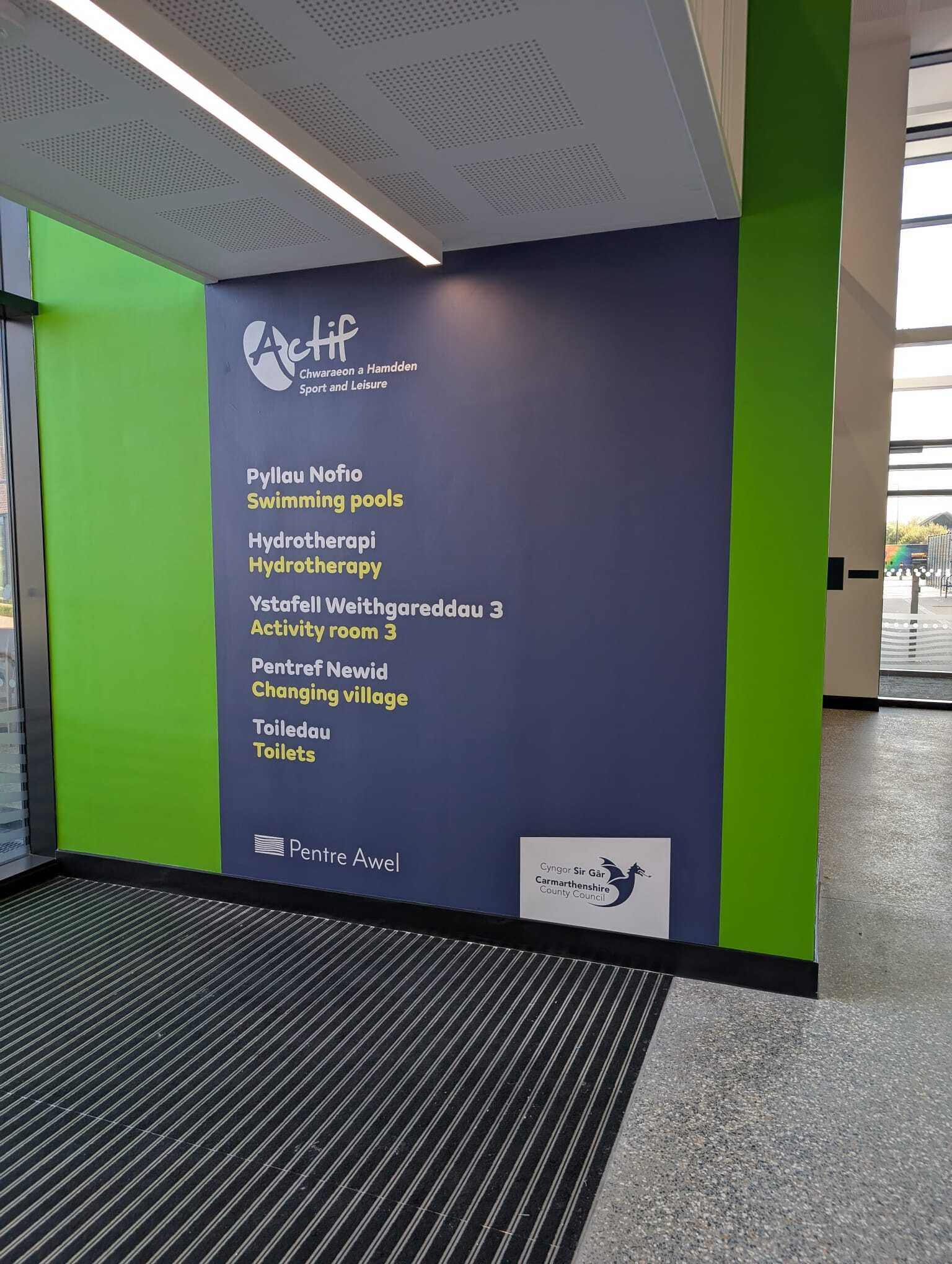 Bilingual wayfinding sign panel listing swimming pools, hydrotherapy and other facilities