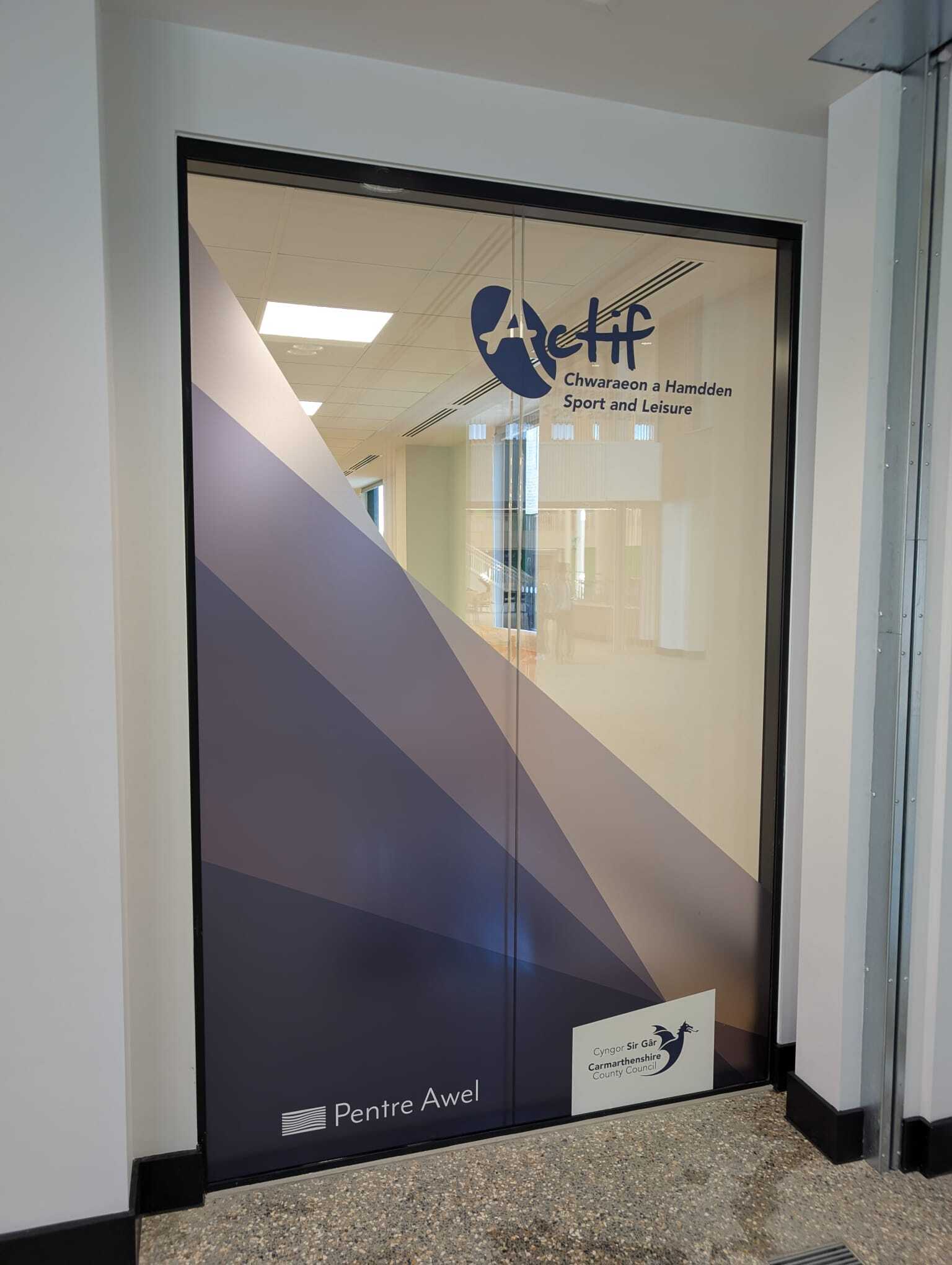 Glass entrance doors with layered diagonal shard graphics in varying print opacities