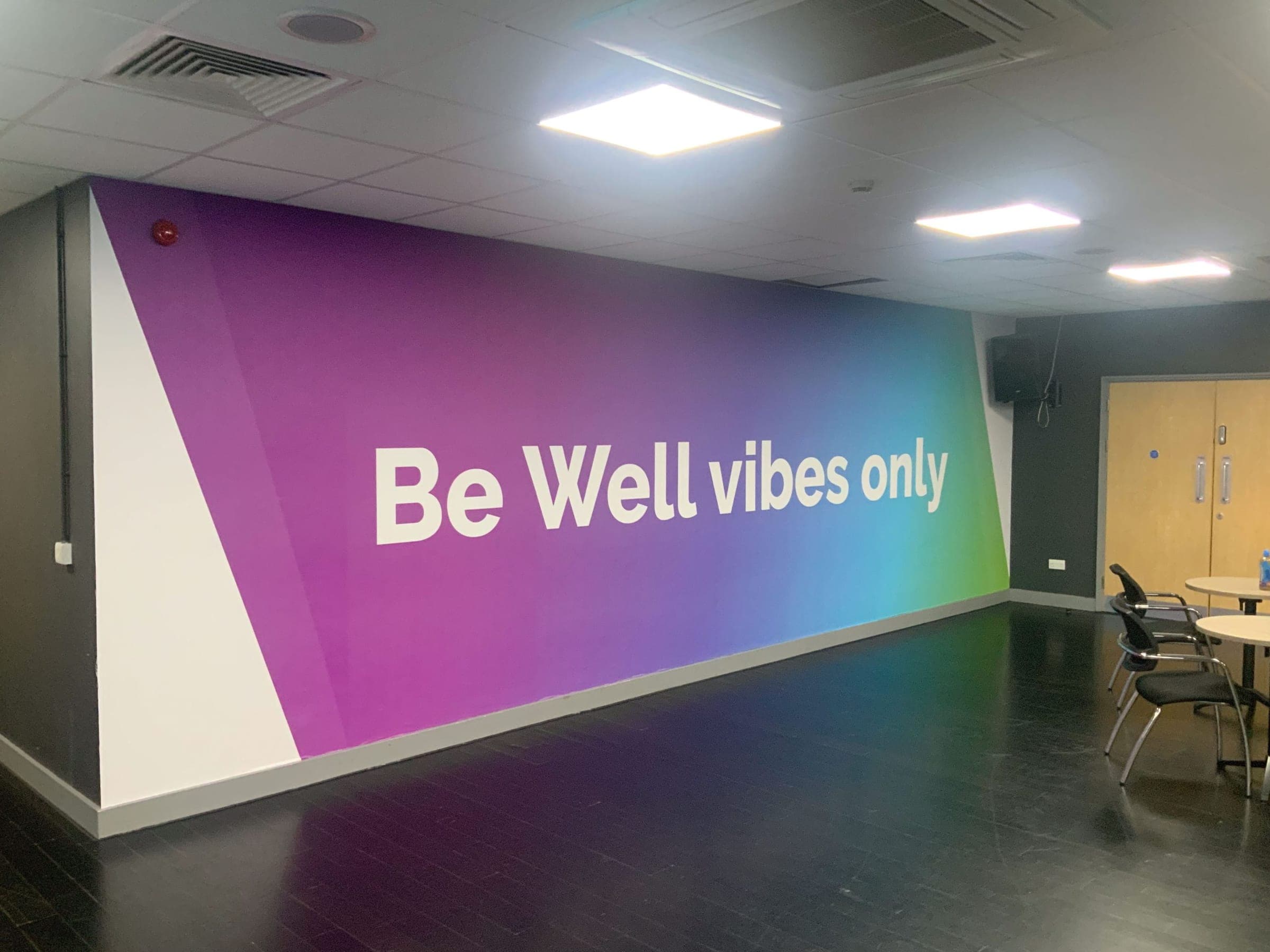 Interior room with full-wall gradient mural reading Be Well vibes only