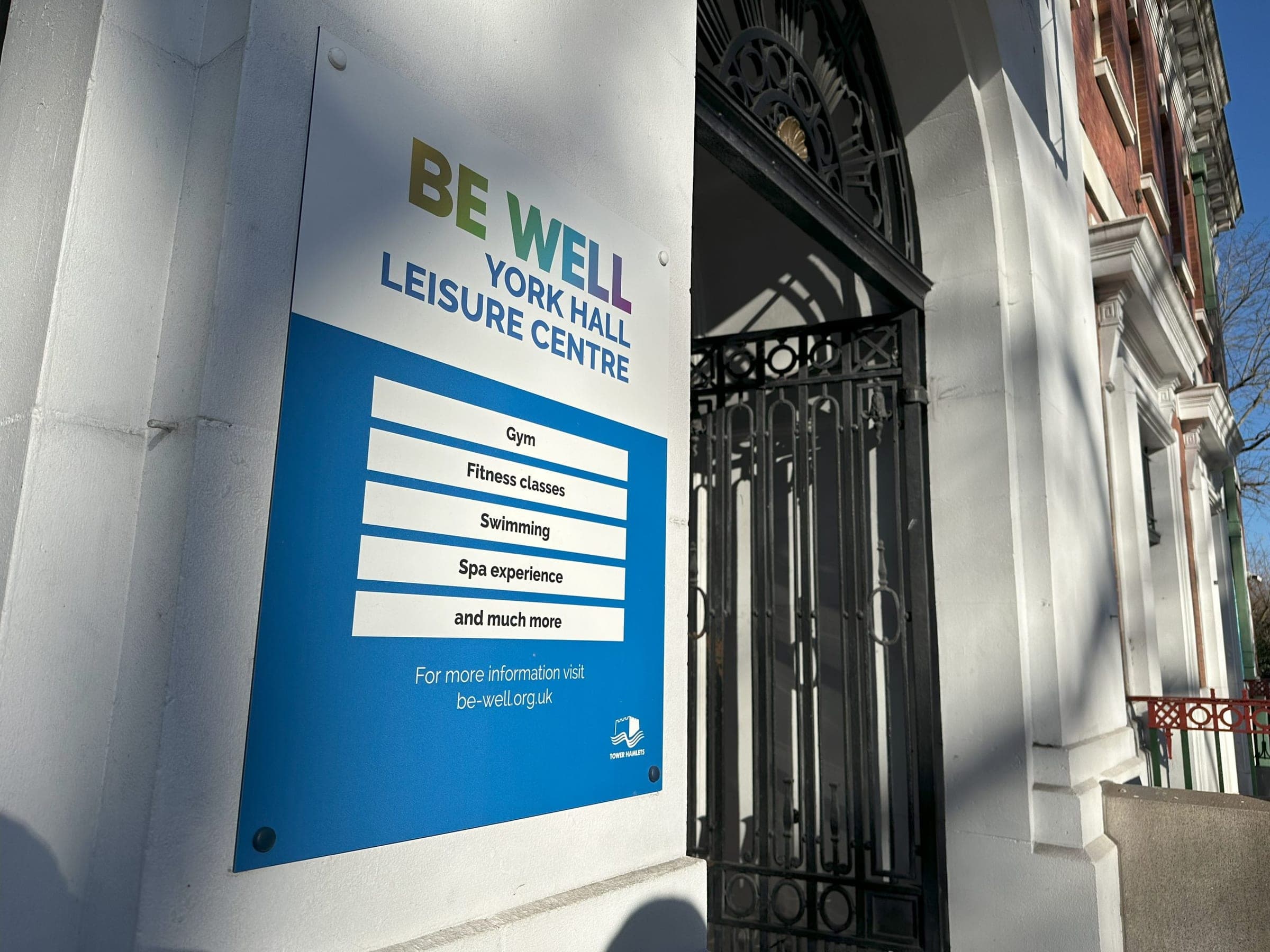 York Hall Leisure Centre facade with Be Well branded services sign listing gym, fitness classes, swimming and spa