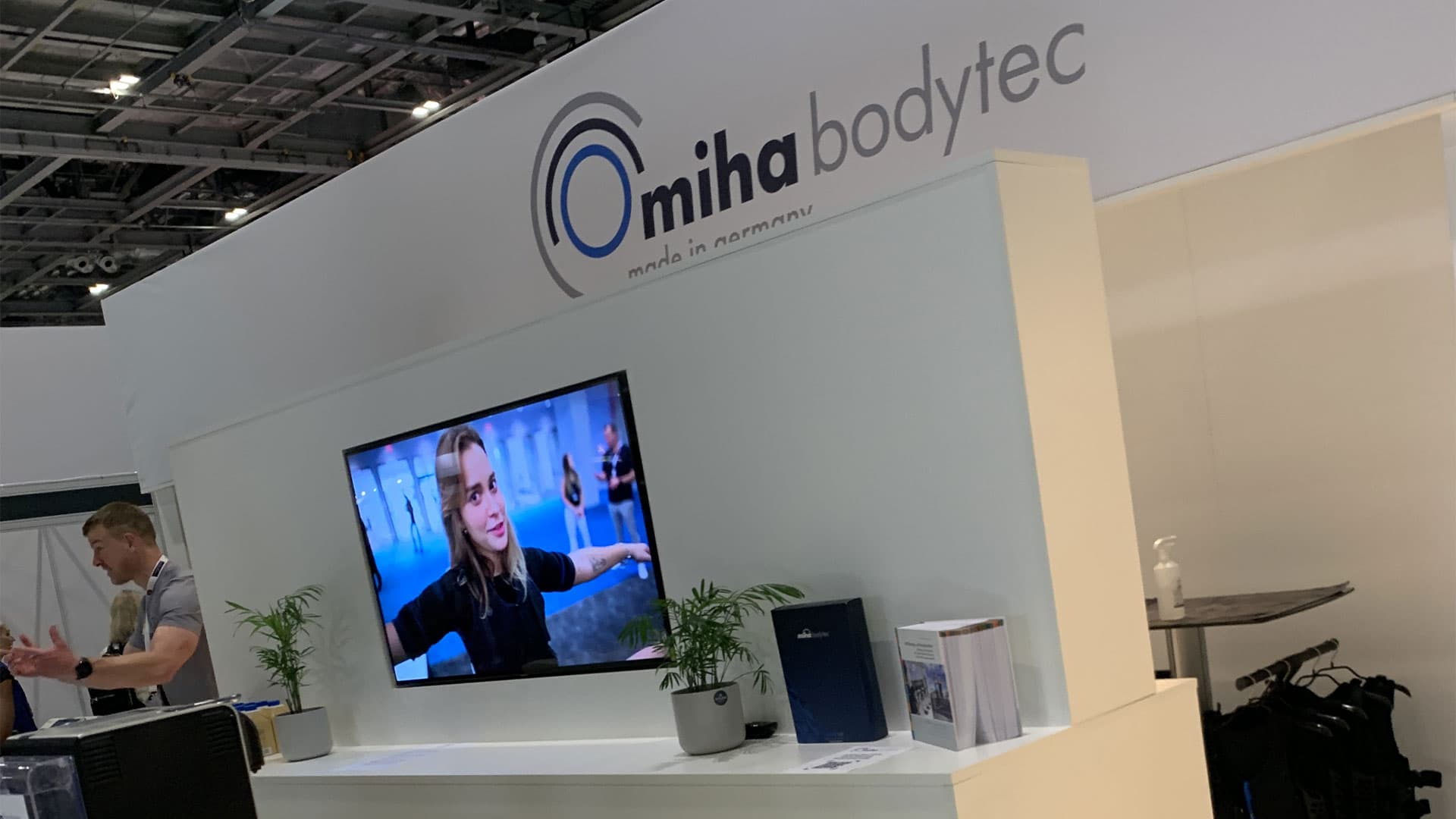 Miha Bodytec exhibition stand fascia with brand logo and wall-mounted product video screen