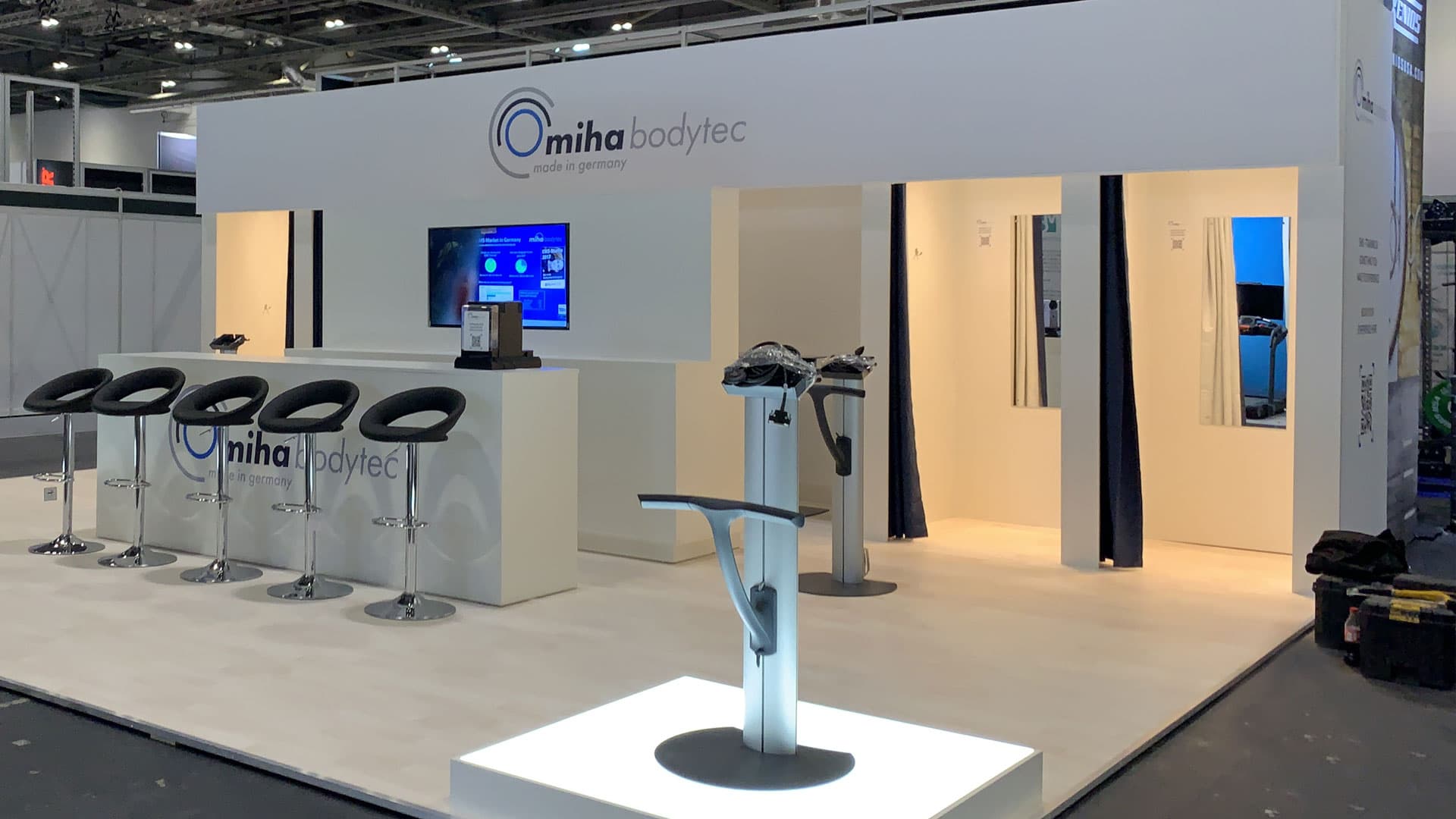 Front-on view of stand at show open with EMS training pedestals on lit plinth and open fitting cubicles