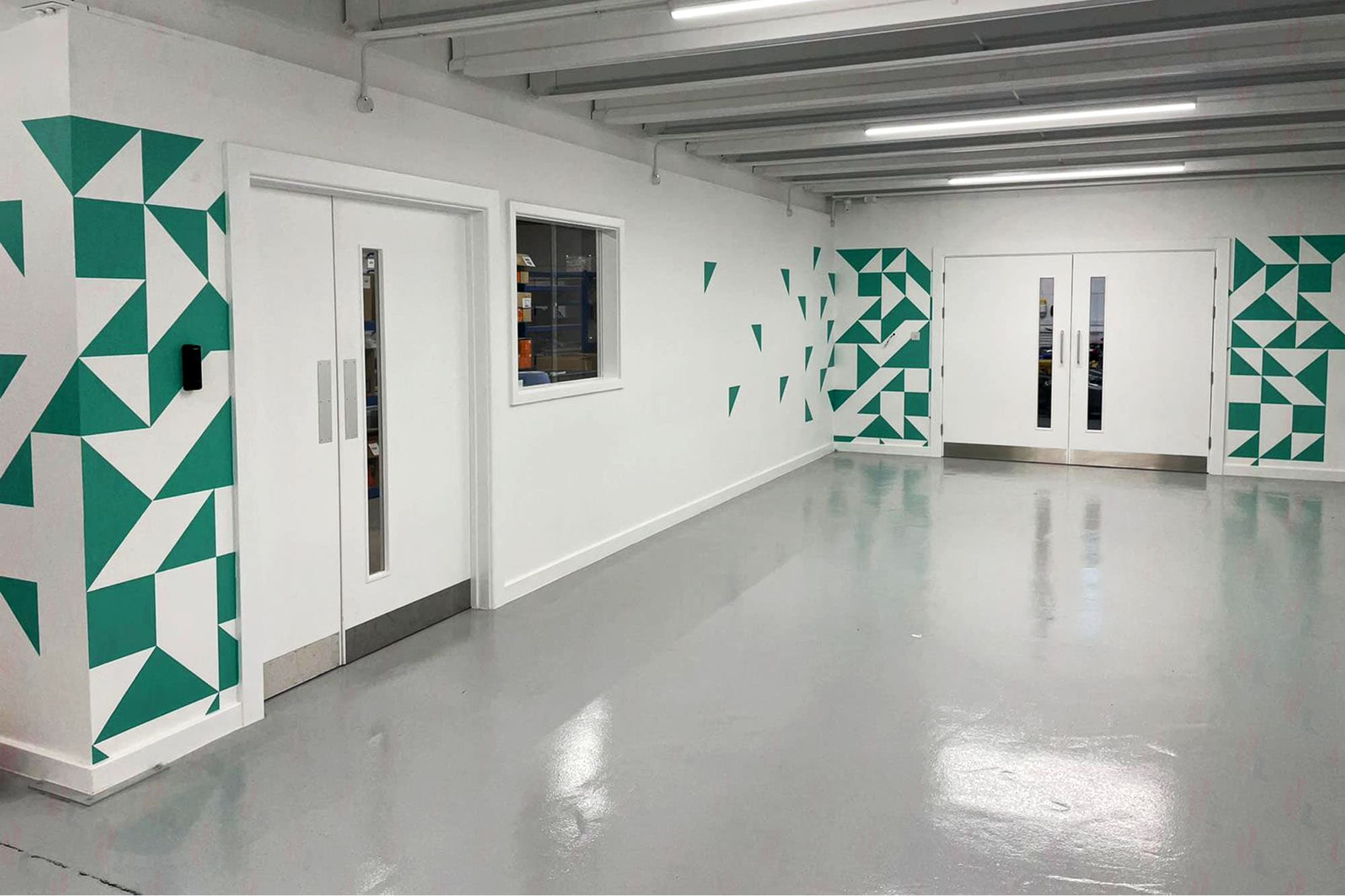 Empty white corridor with teal geometric triangle pattern graphics flanking two sets of double doors