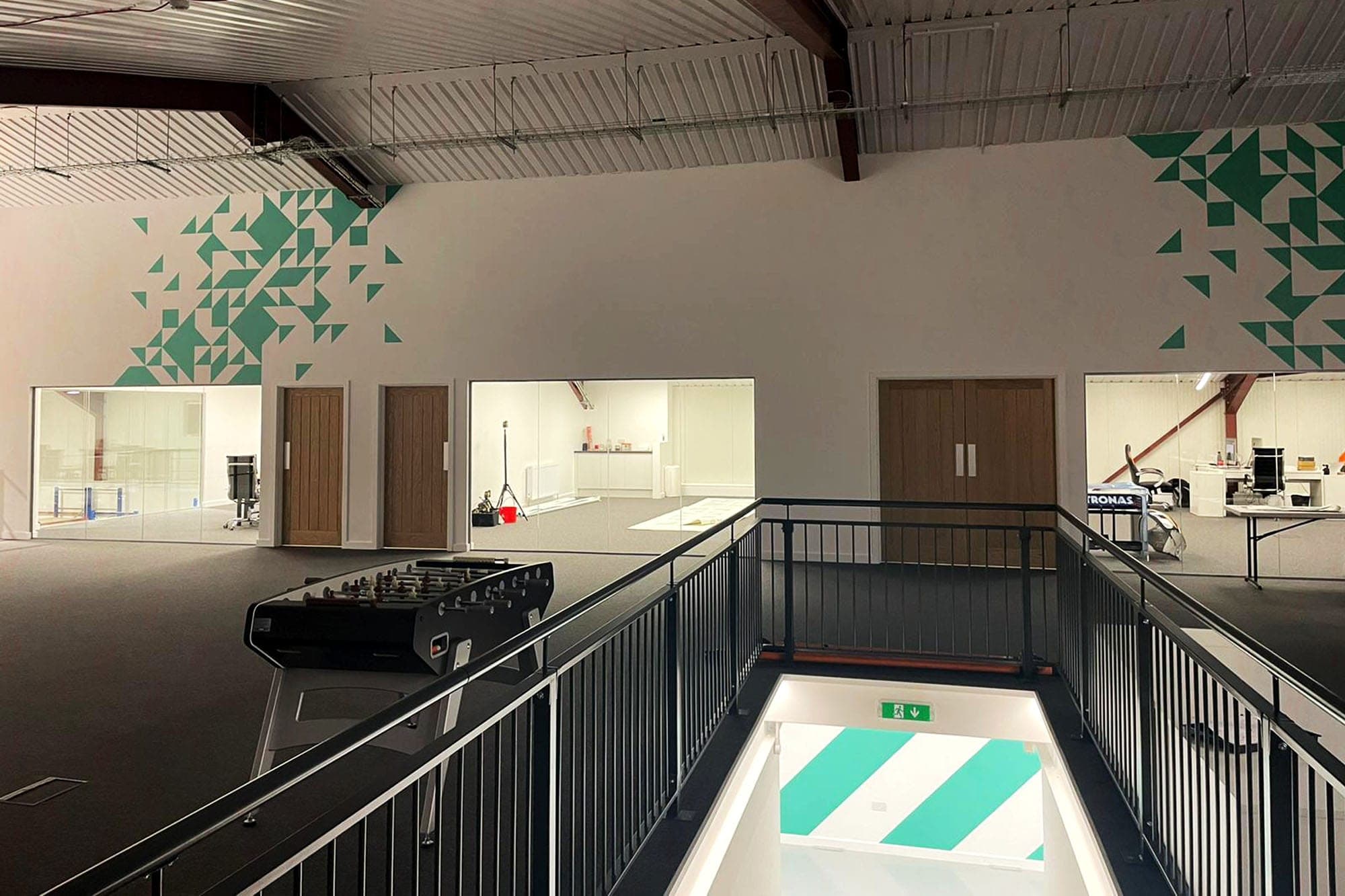 Upper-level view of the large warehouse office with teal geometric murals, foosball table and mezzanine railing